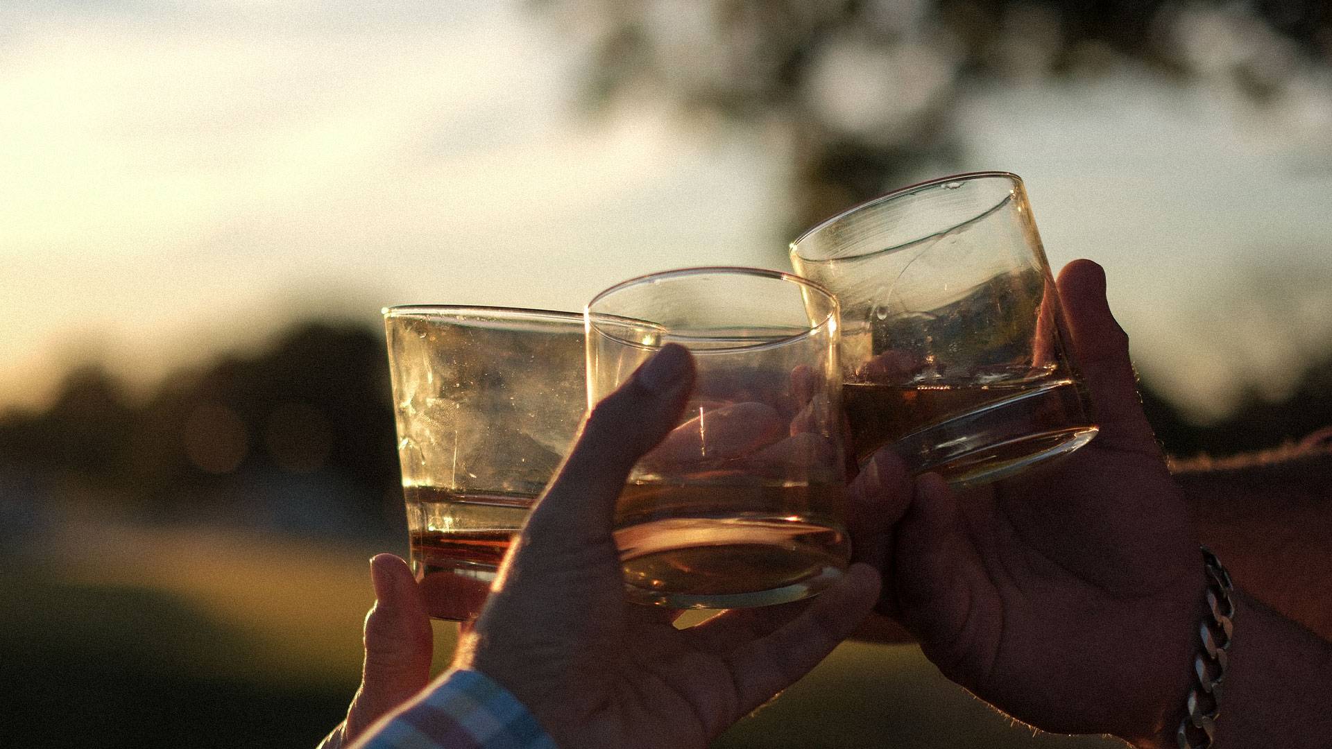 Group of guys doing a cheers with their whiskey glasses with the sun setting in the background