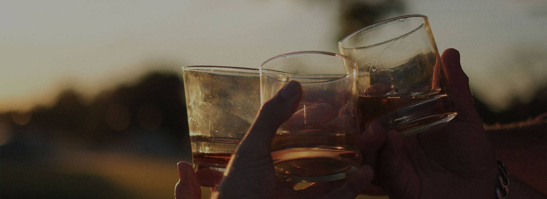 Group of guys doing a cheers with their whiskey glasses with the sun setting in the background