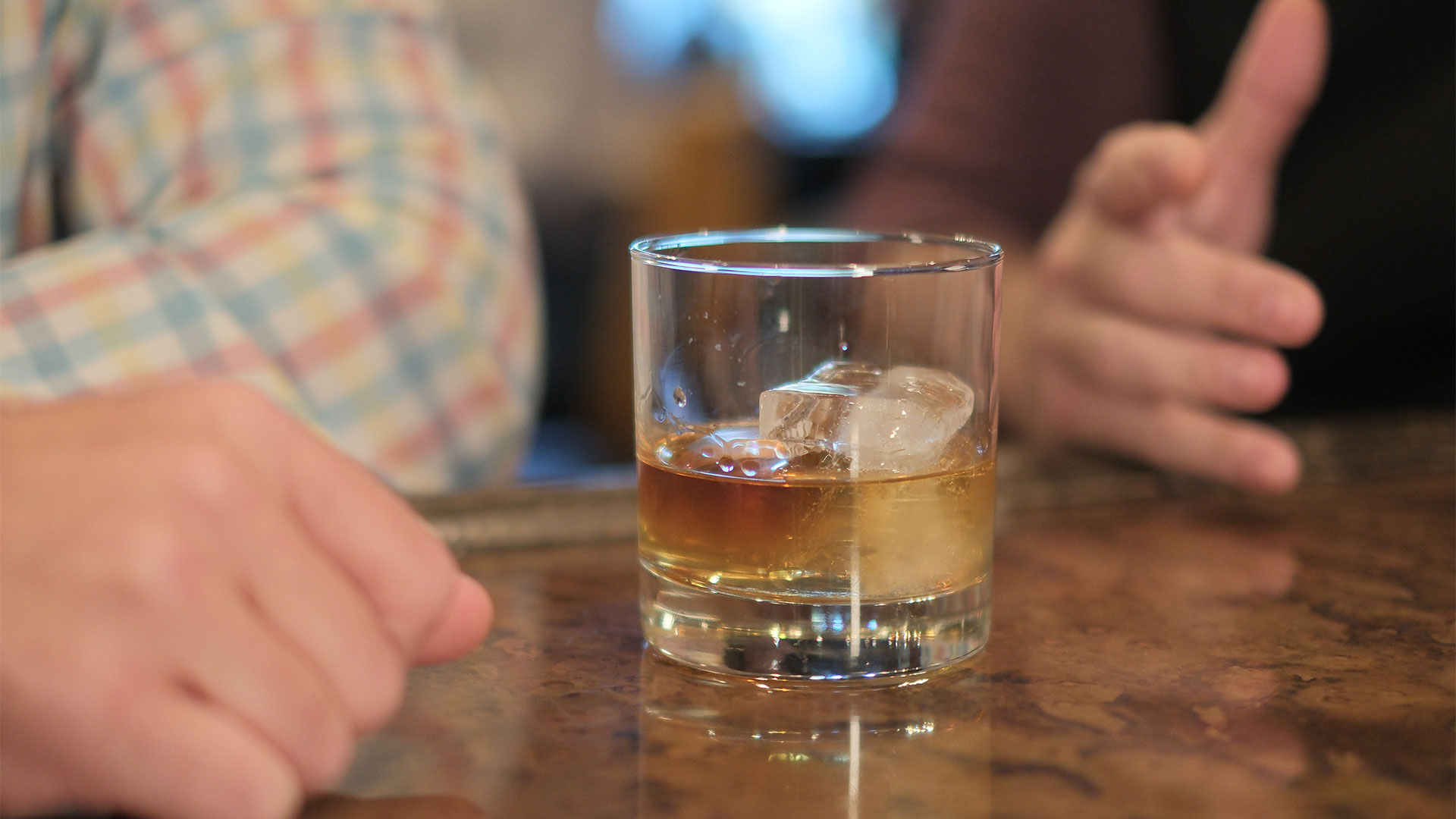 Whiskey glass sitting on bar between two men talking